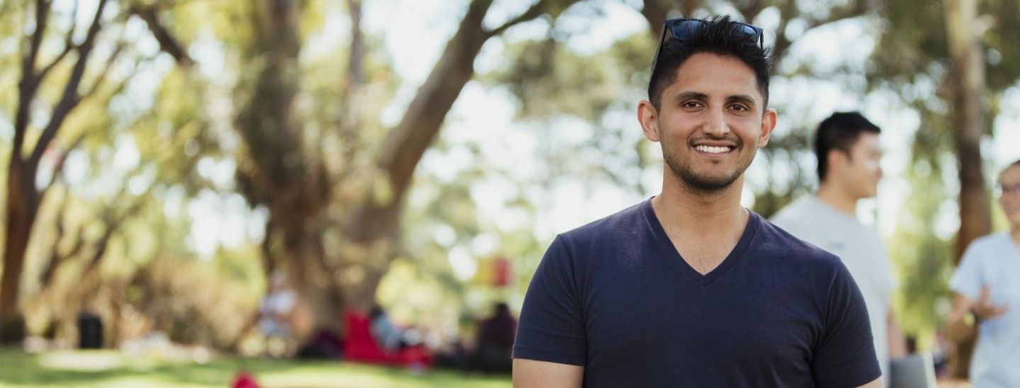 Male student smiling outside holding laptop