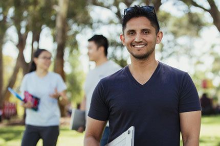 Male student smiling outside holding laptop
