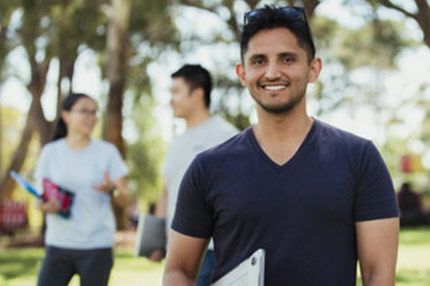 Male student smiling outside holding laptop
